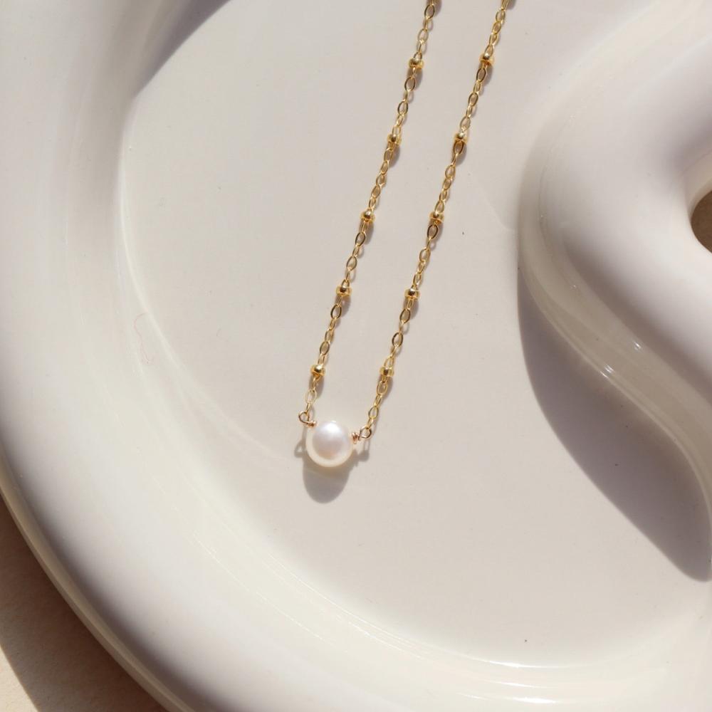 14k gold fill Beaded pearl necklace laid on a white plate in the sunlight