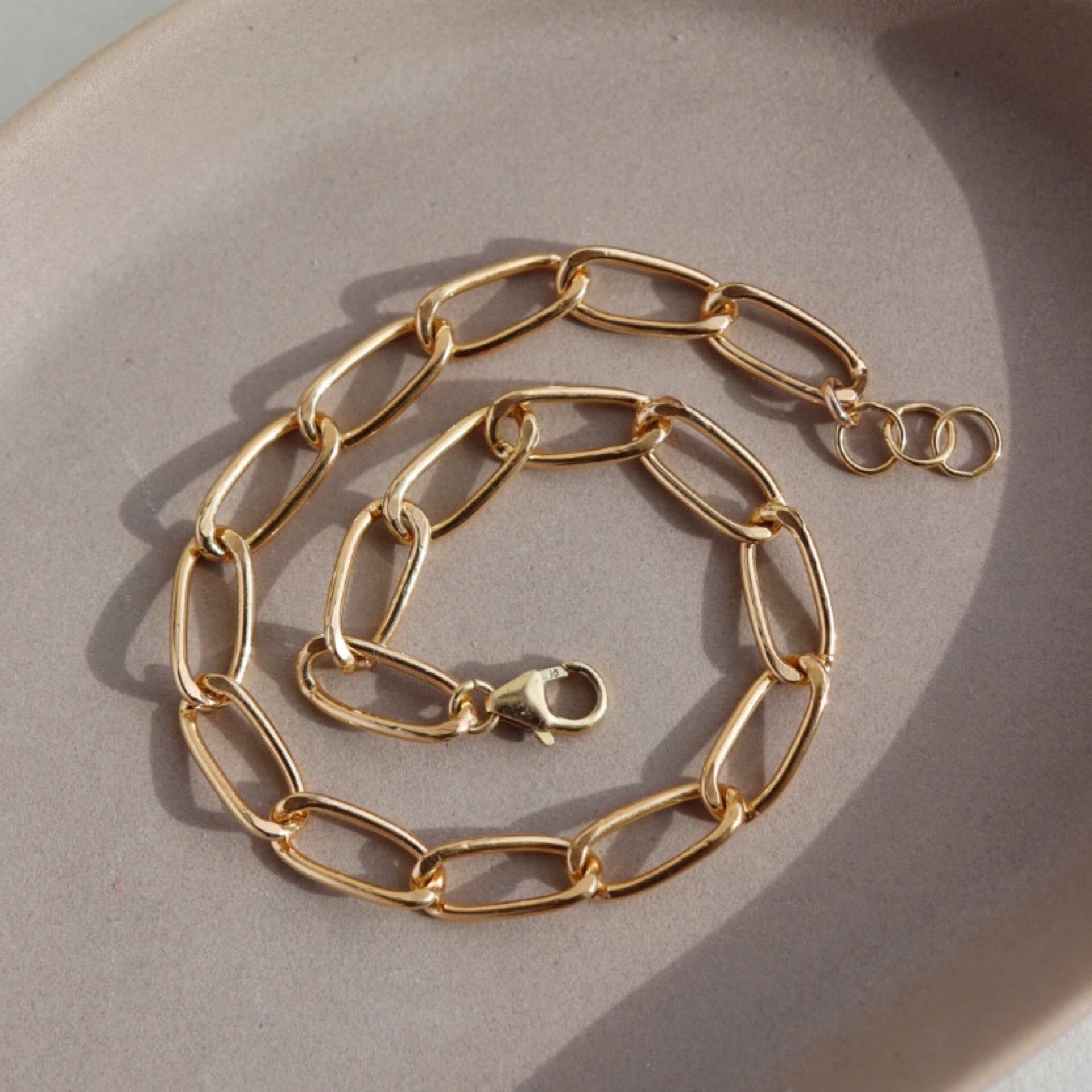 14k gold fill Curve Bracelet sitting on the peach colored plate. Handmade in Eau Claire Wisconsin.
