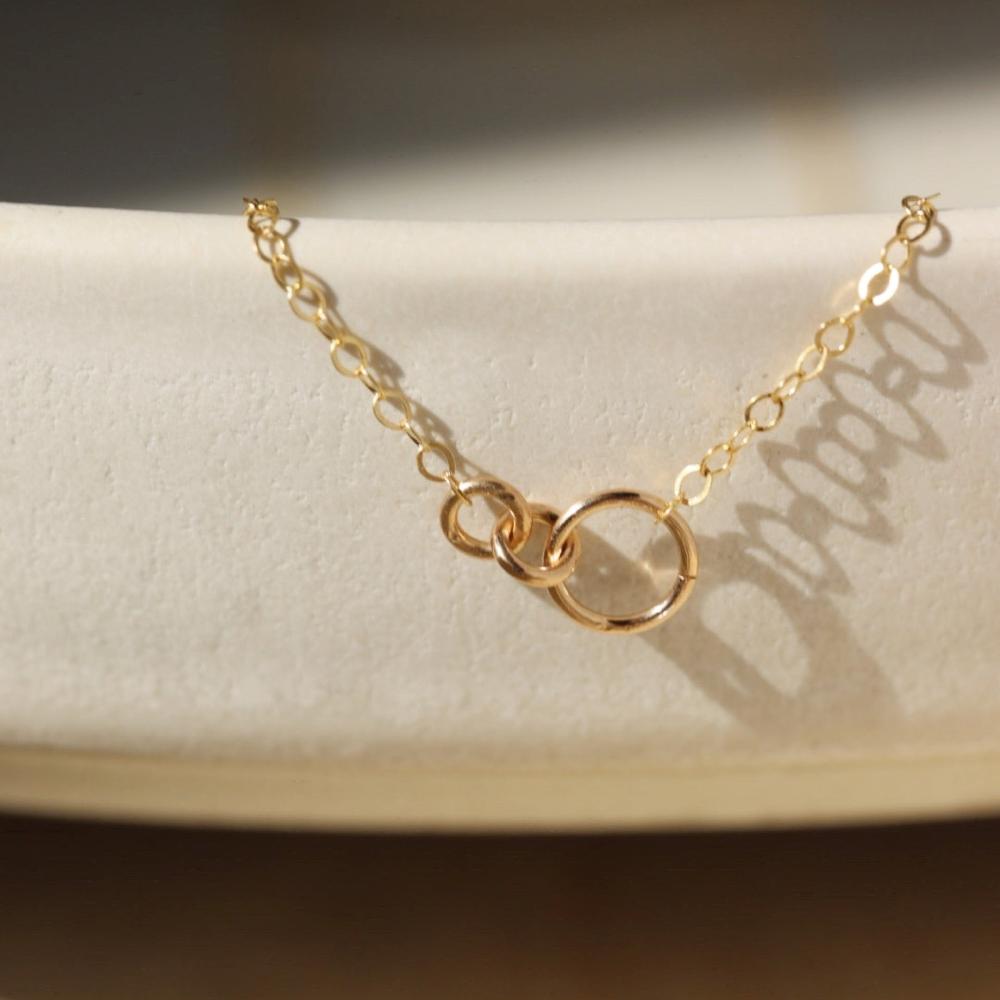14k gold fill Lineage Necklace placed on a white jewelry dish. This necklace features jump rings representing parents, kids, and others you are able to pick the sizing of each jump ring.
