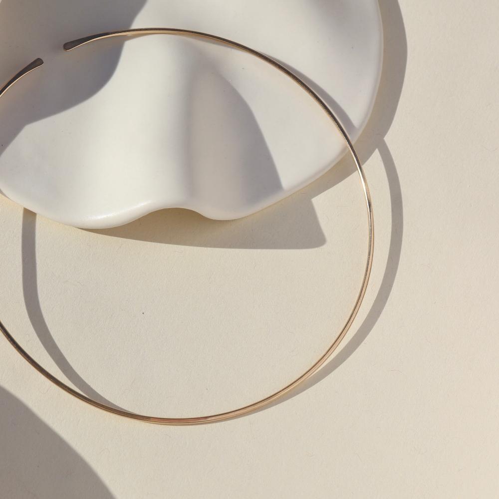 14k gold fill collarbone necklace by token jewelry, laid on a white dish in the sun