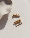 A gold necklace layering clasp with three necklace attachment points laid on a stone plate in the sunlight.
