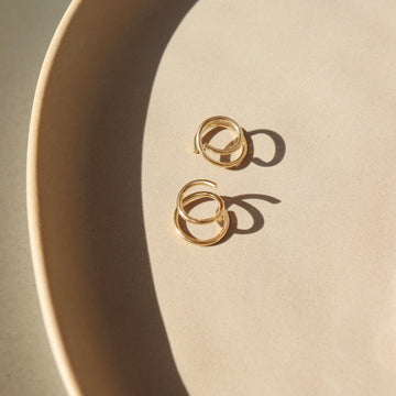 14k gold fill Mini Twist Earrings laid on a peach colored plate in the sunlight. These earring have a little twist giving the allusion that you have two piercings. 