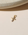 Gold cross charm with clear sparkling stones, photographed on a neutral surface in warm natural light.