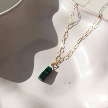 14k gold fill Malachite Necklace laid on a white plate in the sunlight. This necklace features the cossette chain with the Malachite gemstone.
