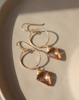 Champagne Quartz Drops laid on a peach colored plate laid in the sunlight. These earrings feature a hook earring with a open circle disc followed my the champagne quartz gemstone.