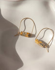 14k gold fill Leopard Skin Jasper Arches placed on a white plate in the sunlight. These earrings feature a hoop like earring with e leopard jasper stone attached to it.