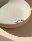 925 sterling silver heritage band sitting on a gray plate in the sunlight. The heritage band Features a lightly hammered band to a high shine.