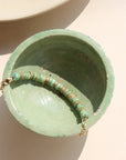 A 14k gold fill beaded anklet with a chain link style chain, draped over a green dish in the sunlight