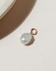 Large freshwater pearl on a round gold fill connector laid on a beige background in the sunlight