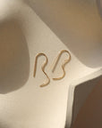 14k gold fill b shaped earrings on a light dish