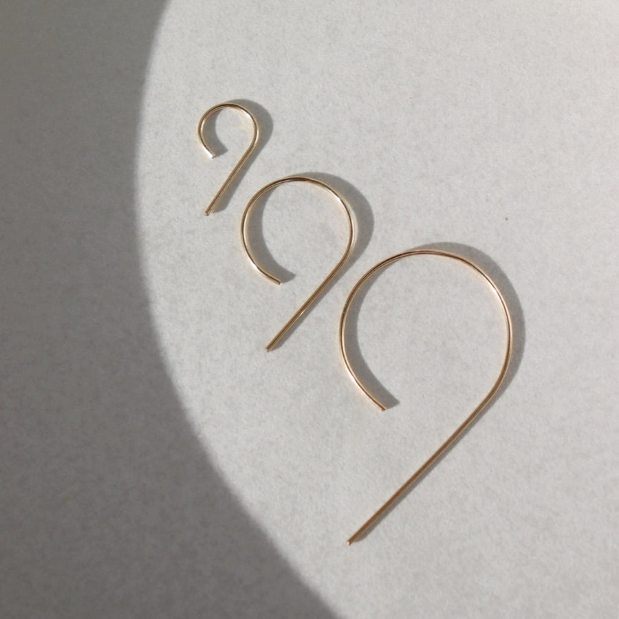 14k gold fill nine earrings laid on a gray plate in the sunlight. These earring give the effect of the number 9.