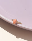 Coral gemstone set in a 14k gold fill bezel, displayed on a purple dish in natural sunlight.