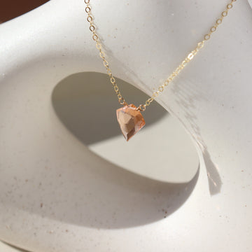 Champagne quartz necklace is laid on top of a white pot. This necklace and pot are placed in the sunlight. This necklace features the Pink Champagne Quartz gemstone connected by the simple chain. This necklace is hand made in Eau Claire Wisconsin.