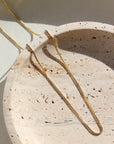 14k gold fill Necklace laid on a cream plate in the sunlight.