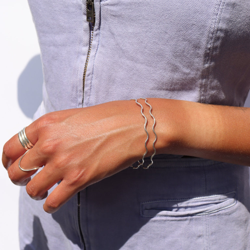 Model wearing two sterling silver bangles with wave-like textured wire