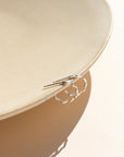 A wave like sterling silver textured huggie earring, displayed on a tan dish in the sunlight.