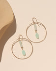 A 14k gold fill hoop with druzy + burma jade gemstones dropping from the ear post. The earrings are displayed on a cream back drop in the sunlight.