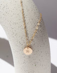 14k gold fill birth flower necklace with round charm on a white plate in the sunlight.