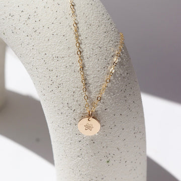14k gold fill birth flower necklace with round charm on a white plate in the sunlight.