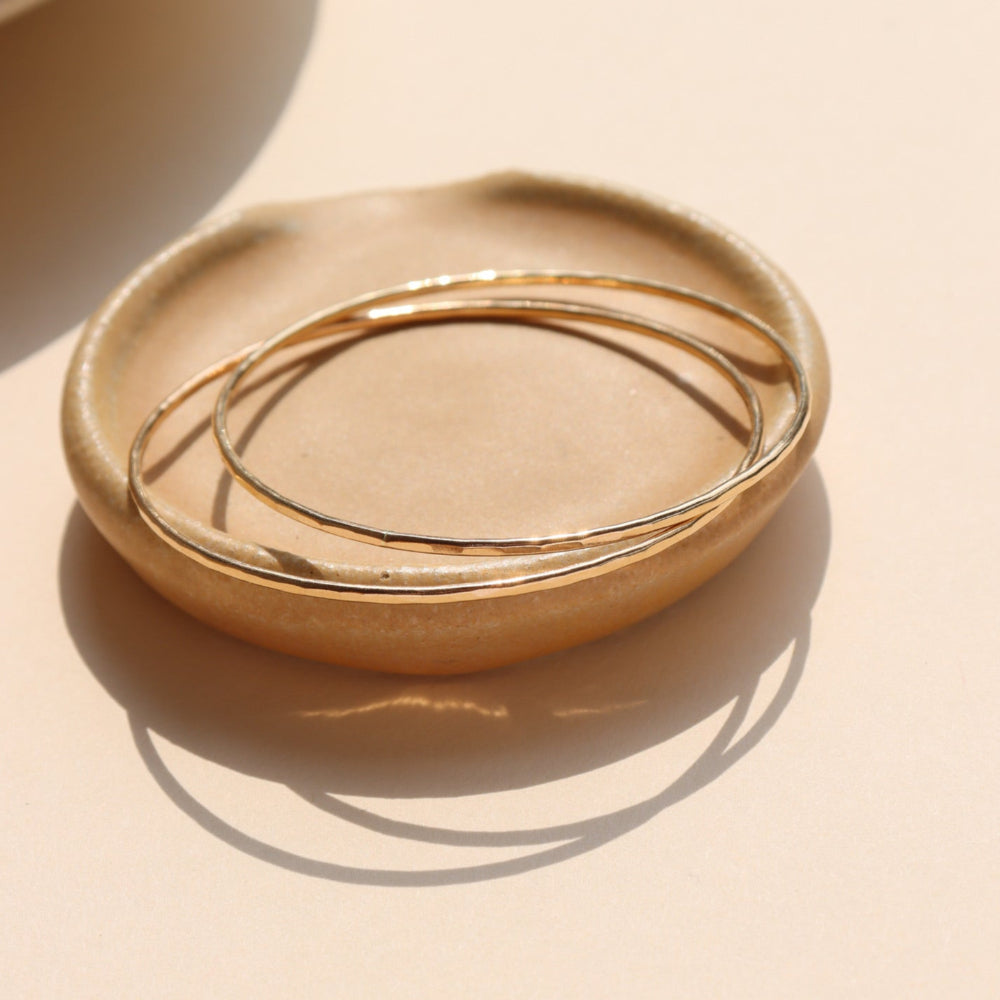 Fine Line Bangle in gold fill and sterling silver, hammered to a shine, shown stacked with other bracelets and worn solo for a minimalist look.