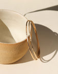 Fine Line Bangle in gold fill and sterling silver, hammered to a shine, shown stacked with other bracelets and worn solo for a minimalist look.