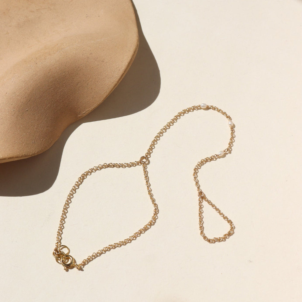 A 14k gold fill rolo hand chain with three margot pearls wire wrapped into the chain. The hand chain is displayed on a. cream back drop.