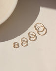 Product photo of Goldie Hoops, 14k gold fill endless hoop earrings in four graduated sizes, displayed on a light surface in warm natural sunlight.
