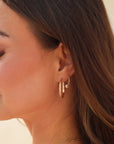 Close-up of a woman wearing gold hoop earrings and a necklace against a neutral background