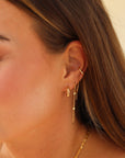 Close-up of a woman wearing gold earrings and necklaces against a neutral background