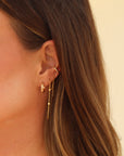 Close-up of a woman wearing gold earrings and necklaces against a neutral background