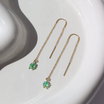 14k gold fill Green Opal Threaders laid on a white plate in the sunlight. These earring feature are a simple chain with a hook earring, green opals dangling on the bottom.