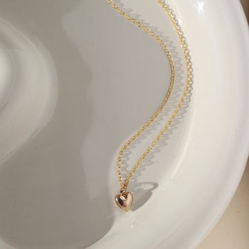 14k Everthine Necklace laid on a white plate sitting in the sunshine, This necklace features the simple chain along with the puff heart. Handmade in Eau Claire, Wisconsin.