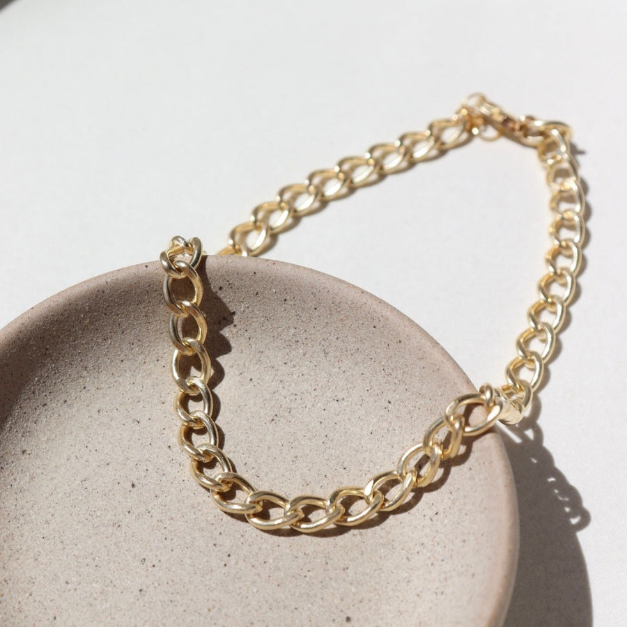 14k gold fill Alexandra anklet laid on a tan jewelry plate in the sunlight.