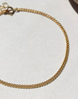 14k gold fill La mer Anklet laid on a white plate in the sunlight.