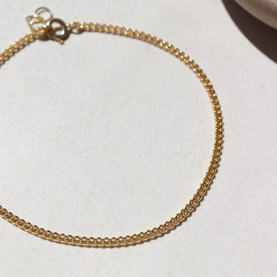 14k gold fill La mer Anklet laid on a white plate in the sunlight.