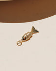 Small gold koi fish charms with red crystal eyes displayed on a neutral surface in warm natural light.
