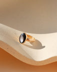 Gold fill floral band with a black mother of pearl gemstone on a beige sand-like surface