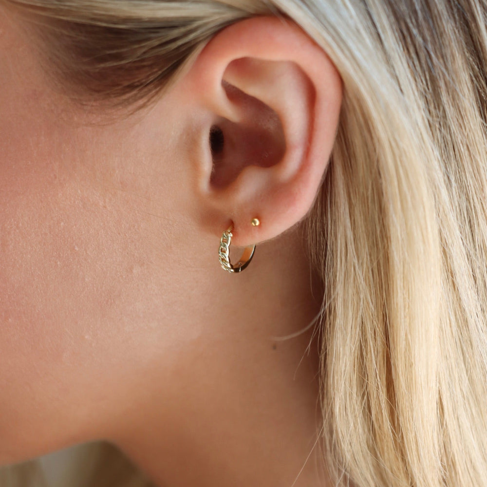 Close-up of a person wearing a gold hoop earring with blonde hair.