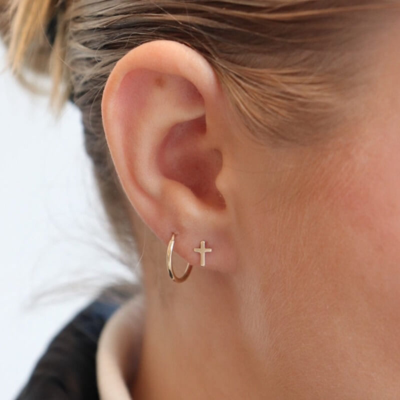Model wearing 14k gold fill cross stud earrings. Along with the classic Goldie  hoops.