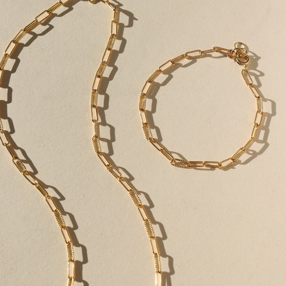 Gold chain necklace and bracelet on a beige background