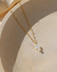 14k gold fill paperclip chain with a mother of pearl cross bead pendant on a light plate