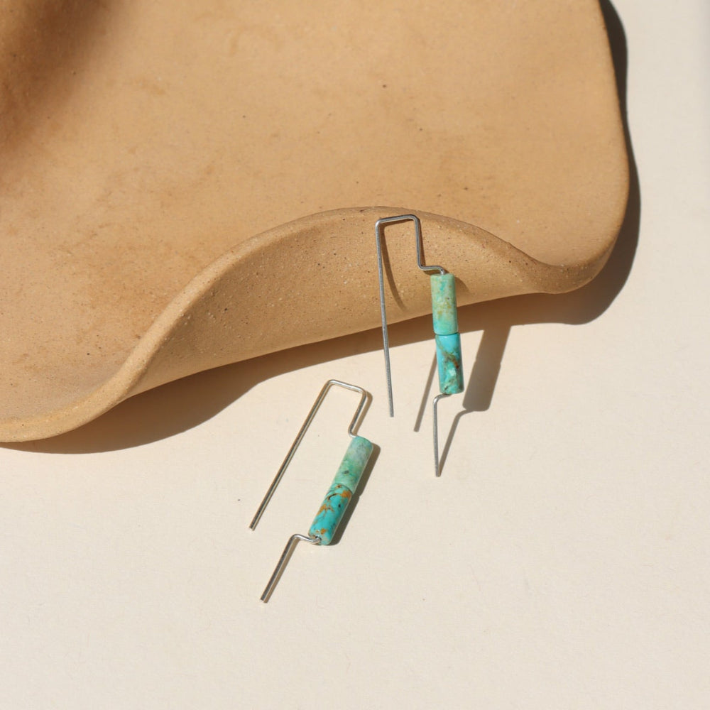 Sterling silver threaders with two turquoise tube shaped gemstones, the earrings are displayed on a cream backdrop
