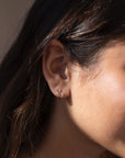 14k gold fill Mini Twist Earrings laid on a peach colored plate in the sunlight. These earring have a little twist giving the allusion that you have two piercings.