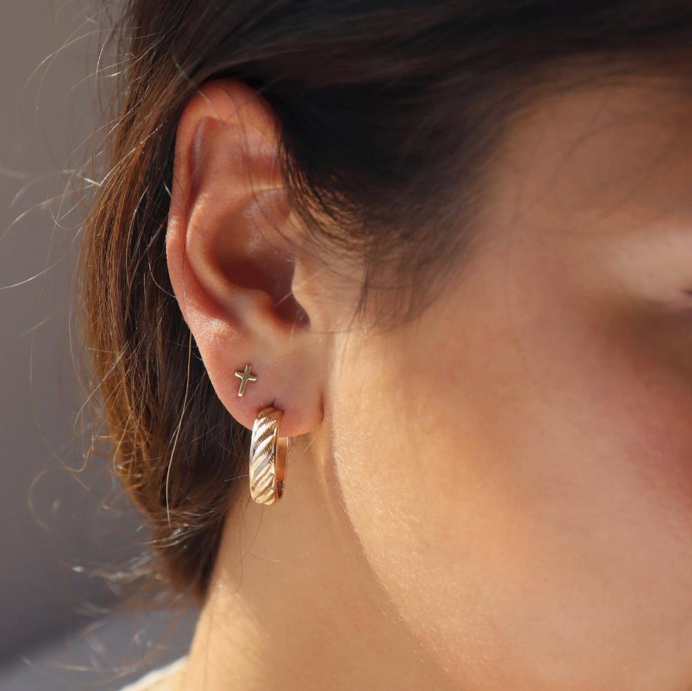 Brunette model wearing 14k gold fill cross studs. Model is also wearing gold ripple hoops.