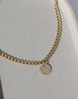 14k gold fill Modern Muse Initial Necklace laid on a tan plate in the sunlight. This Necklace feature our Demi Alexandra chain featuring a charm initial of your choice.