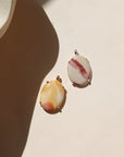 Two oval stone pendants in warm cream, yellow, pink, and red tones set in 14k gold fill and sterling silver, photographed on a cream background in warm sunlight.