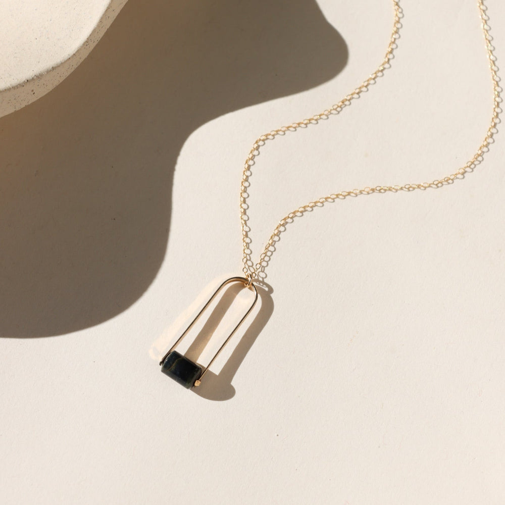 Sable Pendant featuring a smooth blue tiger’s eye gemstone framed by a gold arch