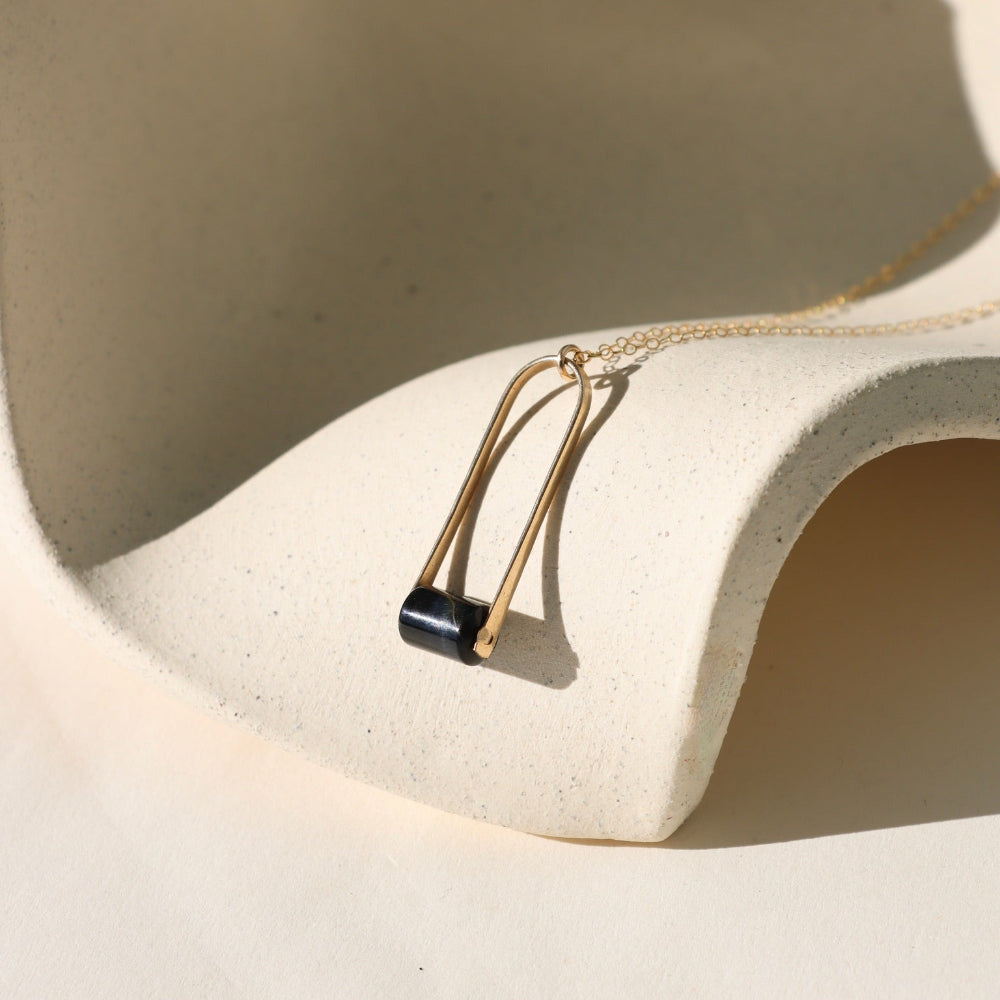 Sable Pendant featuring a smooth blue tiger’s eye gemstone framed by a gold arch