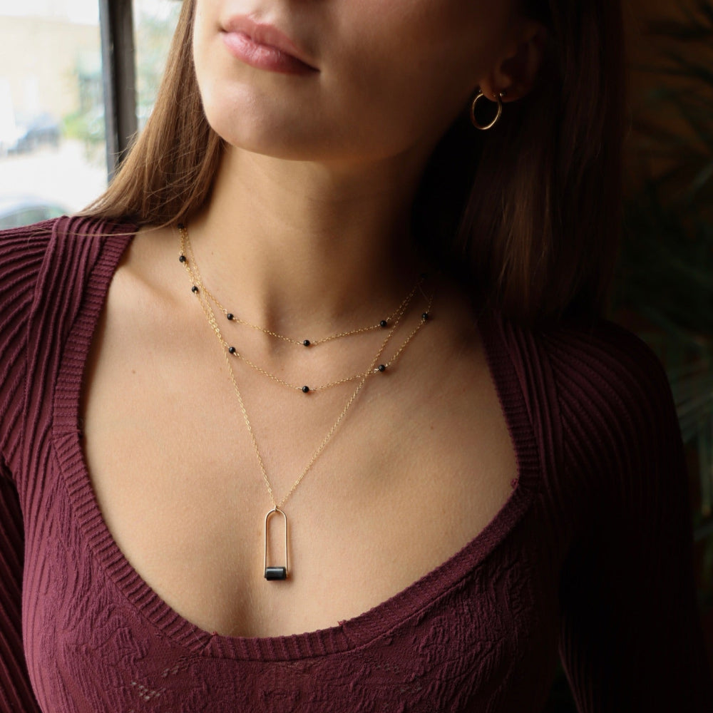 Sable Pendant featuring a smooth blue tiger’s eye gemstone framed by a gold arch