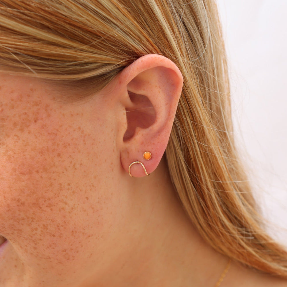 Model wearing Sienna Studs featuring 4mm fiery orange spiny oyster cabochons in 14k gold filled bezel settings.